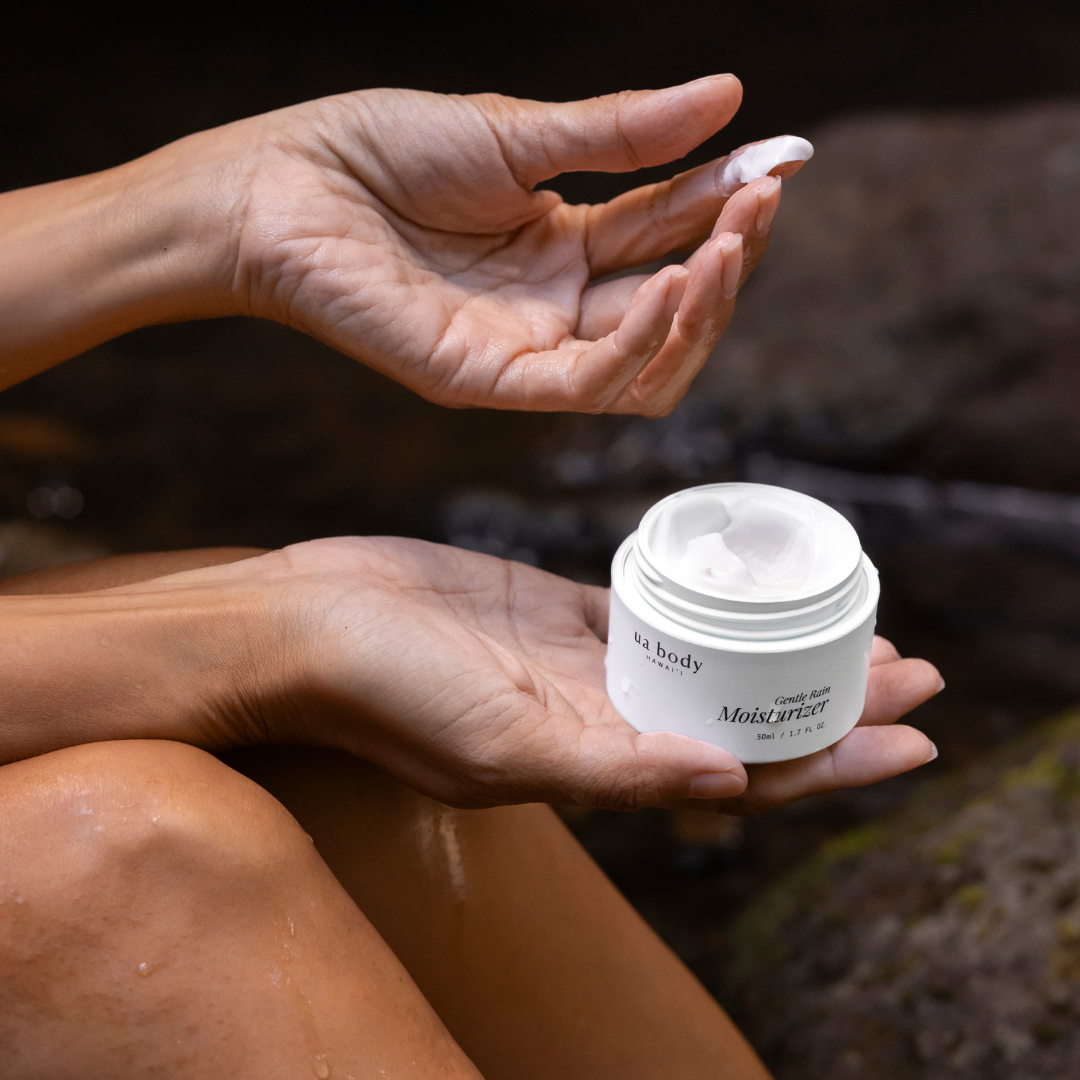 Woman sitting down and holding moisturizer with cream on finger